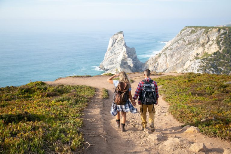 a man and woman walking on a path by a beach