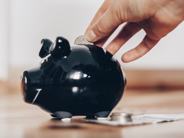 A hand putting a coin into black piggybank